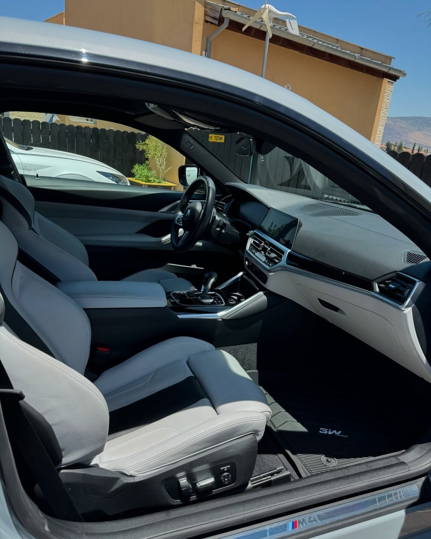 תא הנהג של BMW M4 עם מושבים בהירים ולוח מחוונים, דלת פתוחה