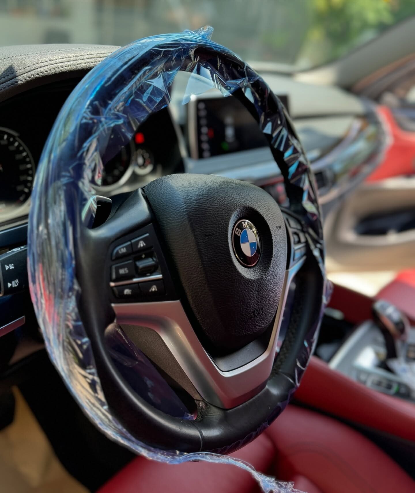 הגה BMW X6 עטוף בניילון שקוף ומושב עור אדום ברקע